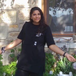 United Vision Türkiye's Facilitator for EU Projects Mrs. Buse Demir standing in a blue dress in front of a wall wearing a wrist watch