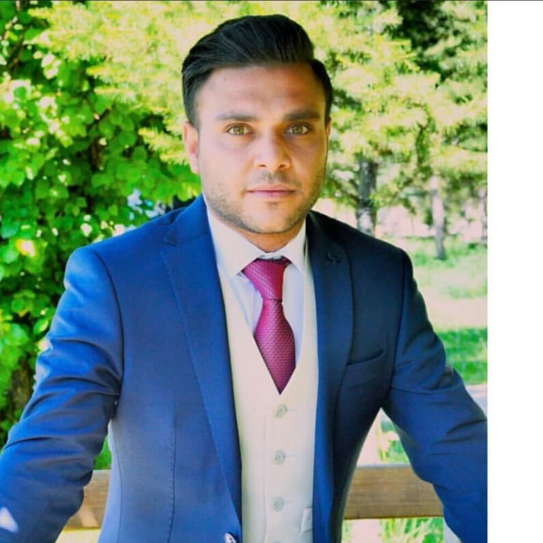 United Vision Türkiye's Coordinator Zawar Hussain stands wearing three-piece blue suit and red tie